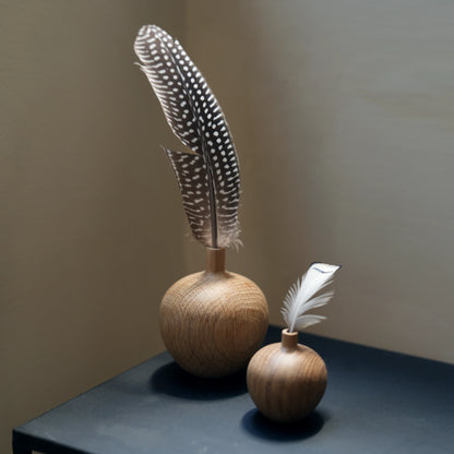 Two oak vases with spotted guinea fowl feathers on a black table.