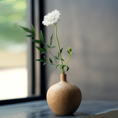 A large oak bud vase with a single white flower on a windowsill.