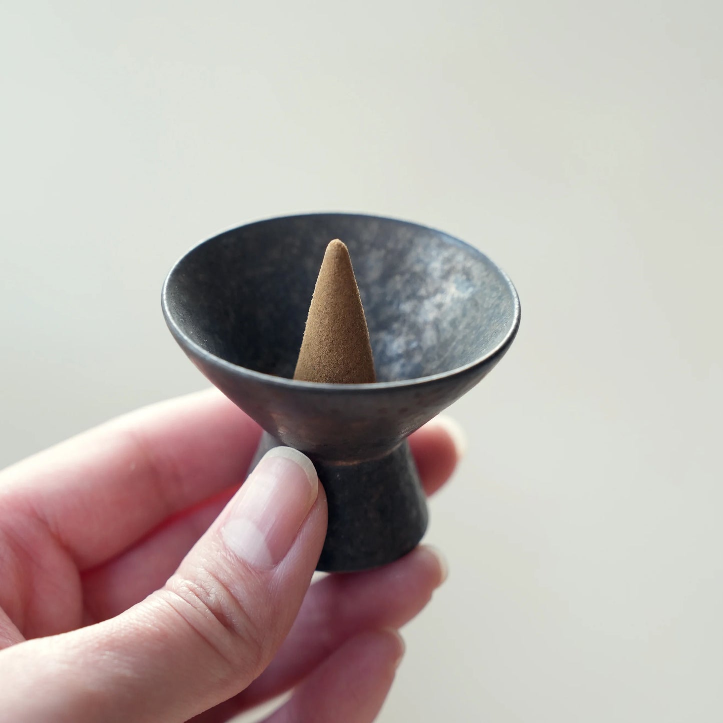 Hand holding a small, dark ceramic incense cone holder.