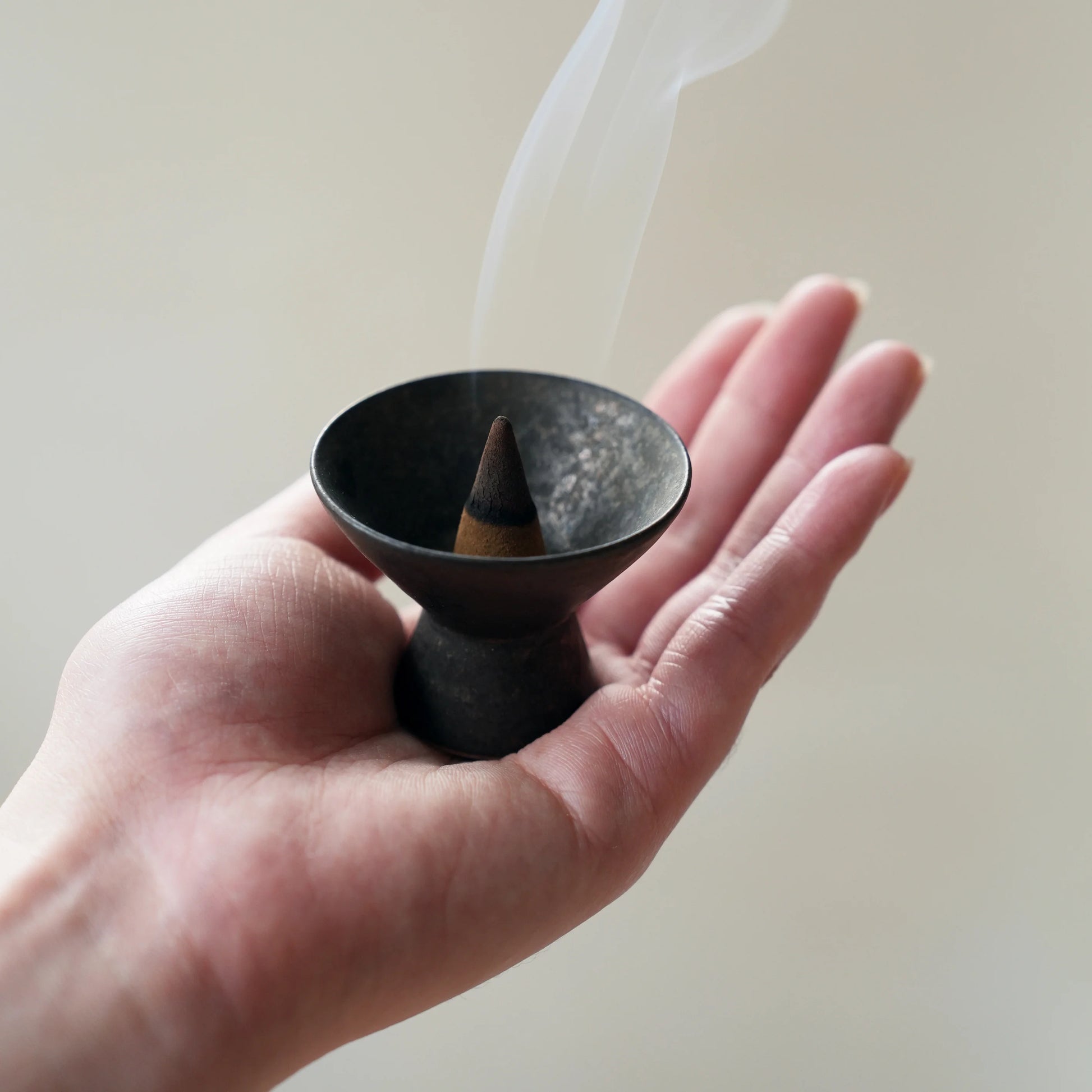 Small ceramic cone incense burner with smoke, held in an open palm.