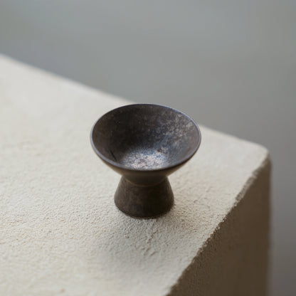 An empty miniature ceramic cone incense burner on a concrete ledge.