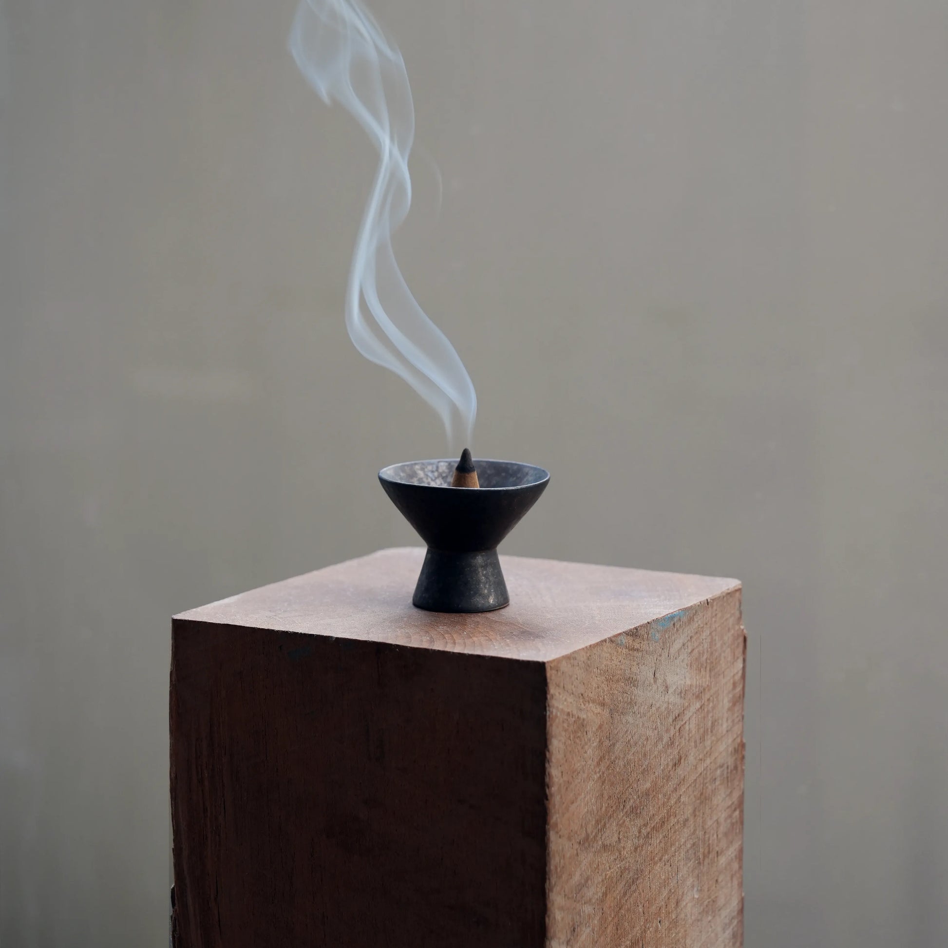 Incense burner with smoke on a wooden block against a plain background