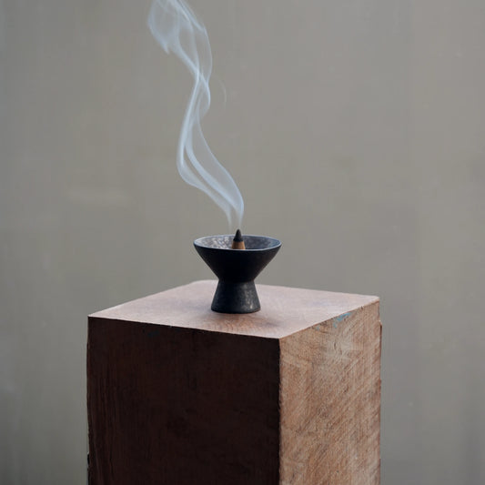 Incense burner with smoke on a wooden block against a plain background
