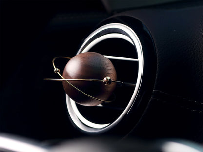 A sculptural walnut car air freshener in a modern car with black interior.