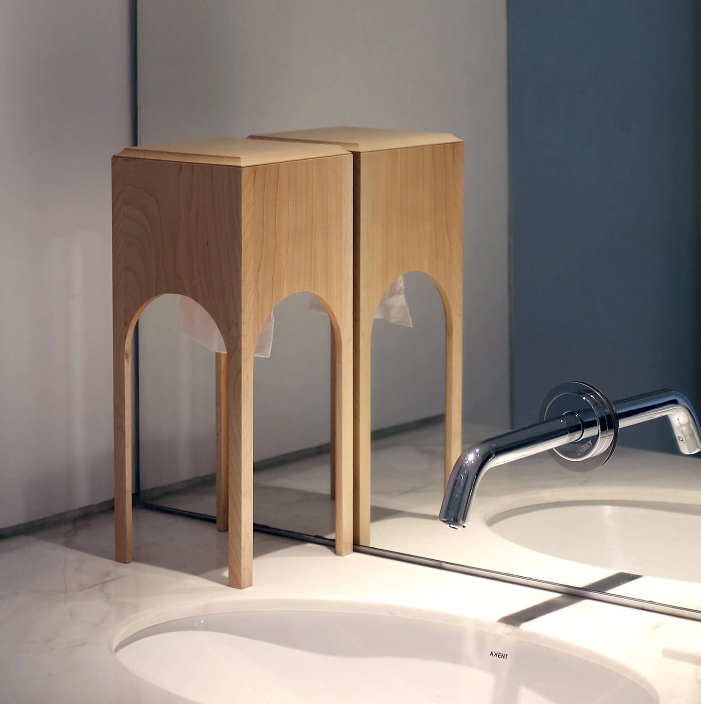 A maple wood tissue box reflected in a mirror on a bathroom vanity.