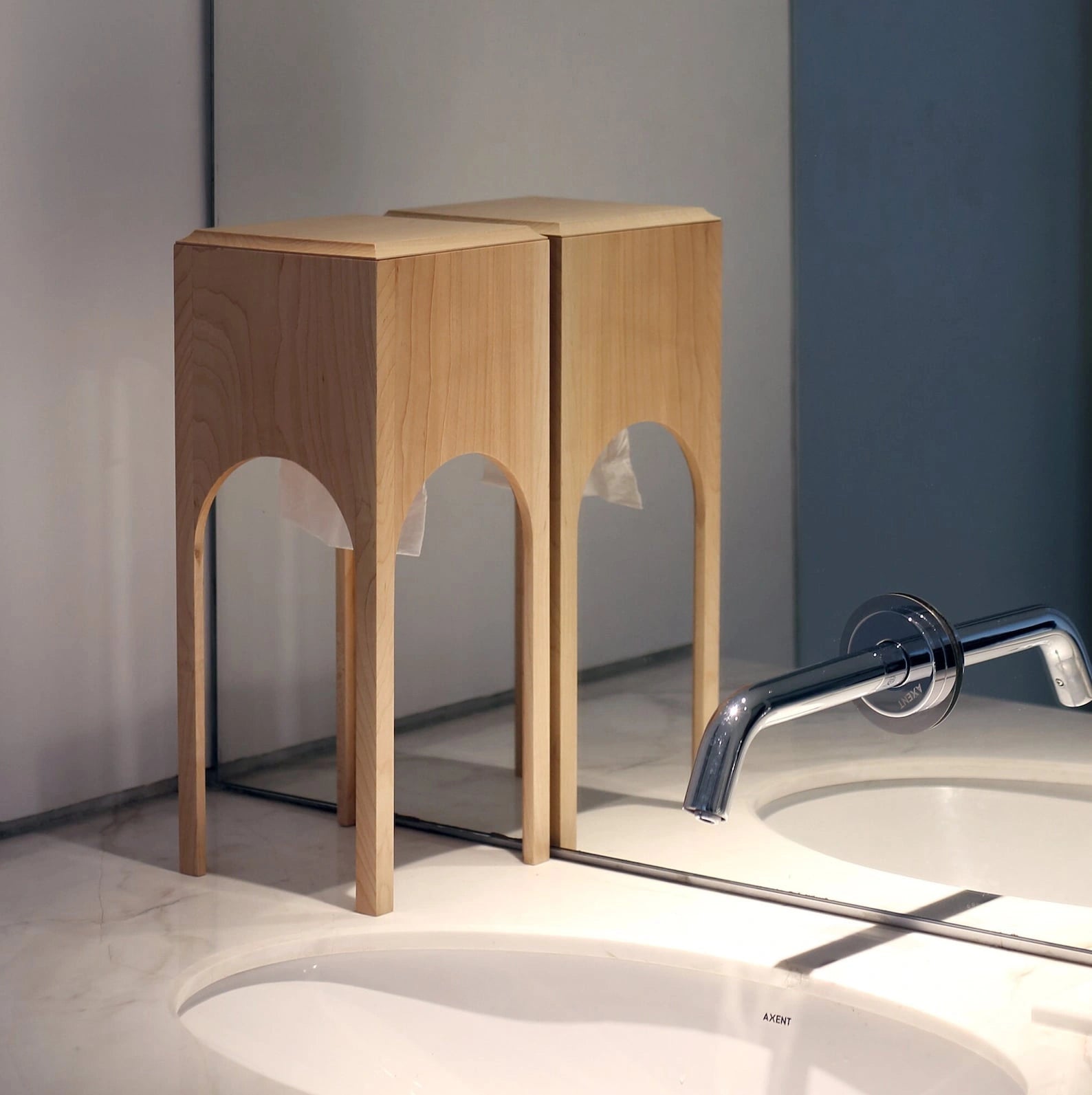 A maple wood tissue box reflected in a mirror on a bathroom vanity.