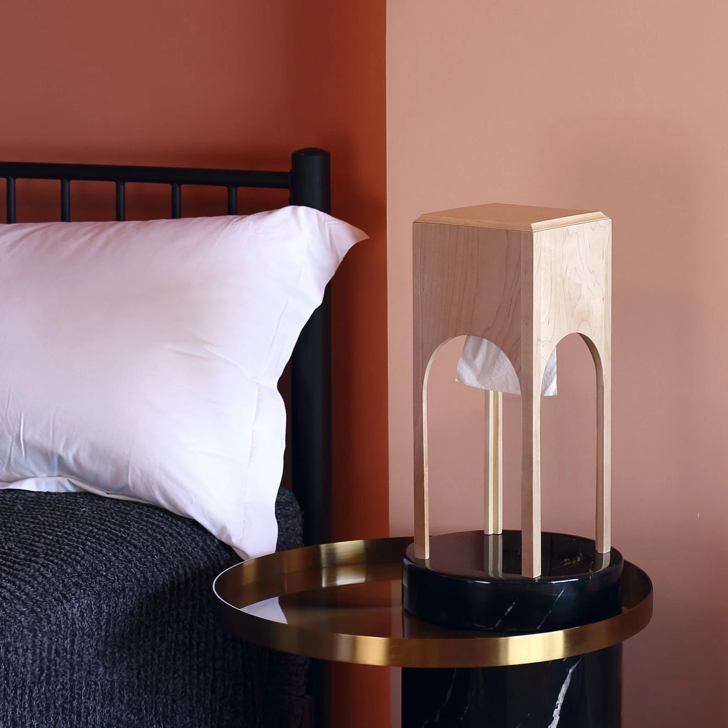 A modern maple tissue dispenser on a black and gold side table.