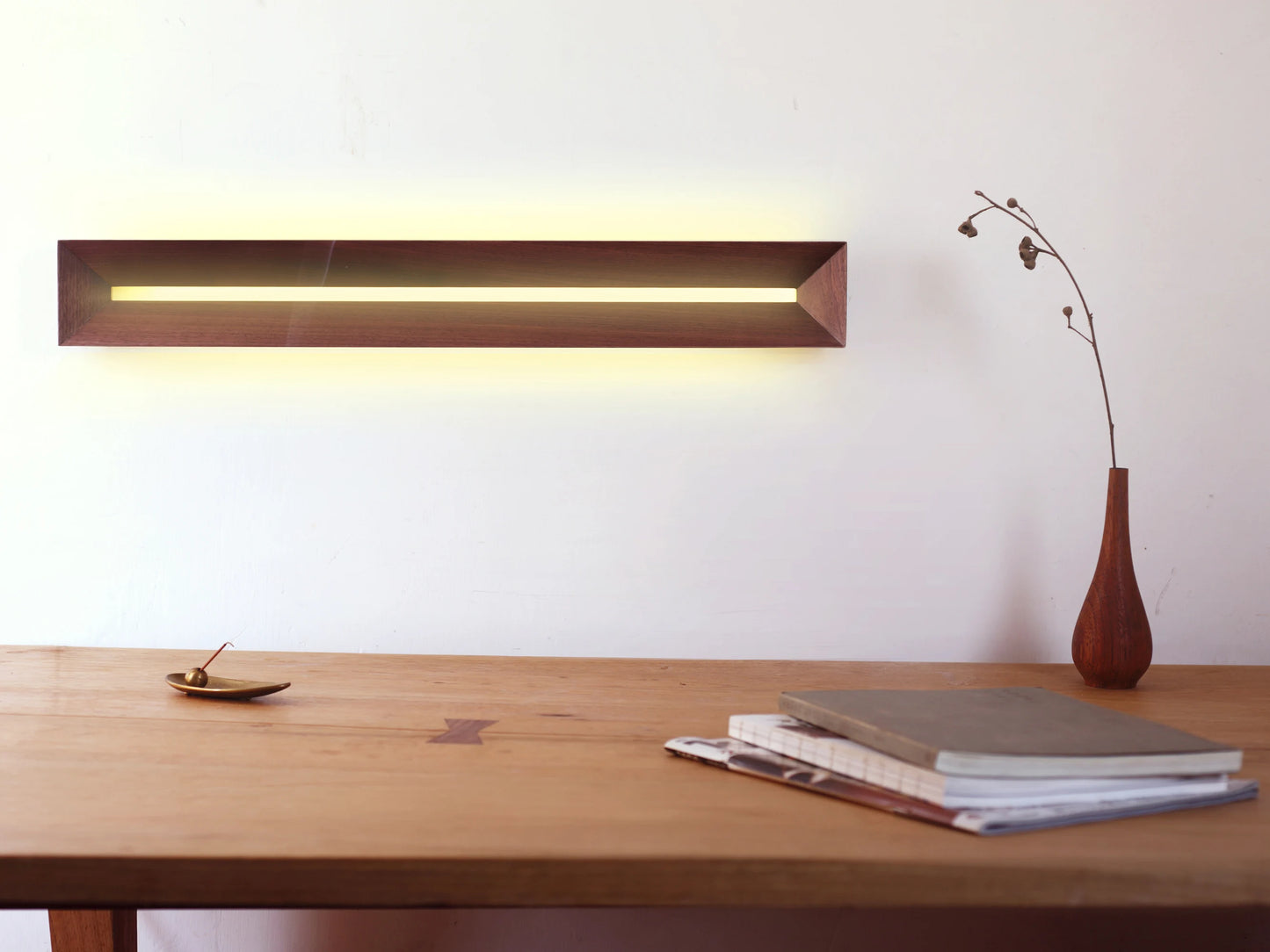 A horizontal walnut wall light mounted above a minimalist wooden desk.