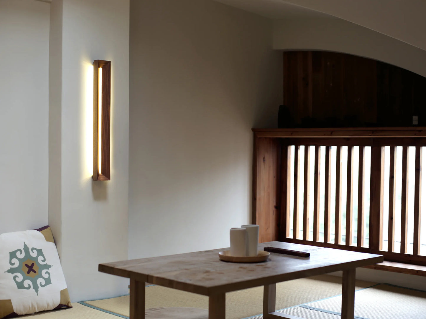 A modern walnut wall sconce mounted vertically in a Japandi-style living room.