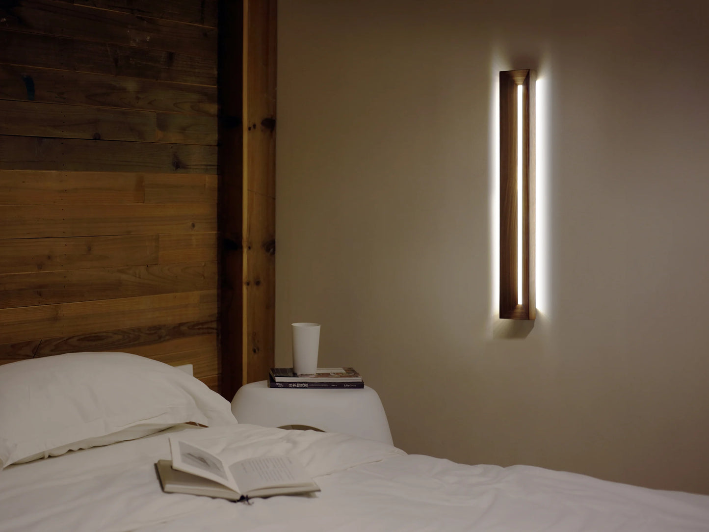 A vertical walnut wall sconce providing warm ambient light in a modern bedroom.