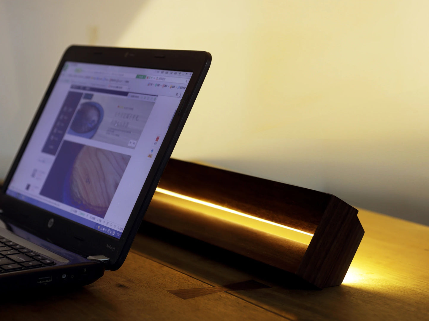 The horizontal wood lamp providing soft, warm light behind a laptop.