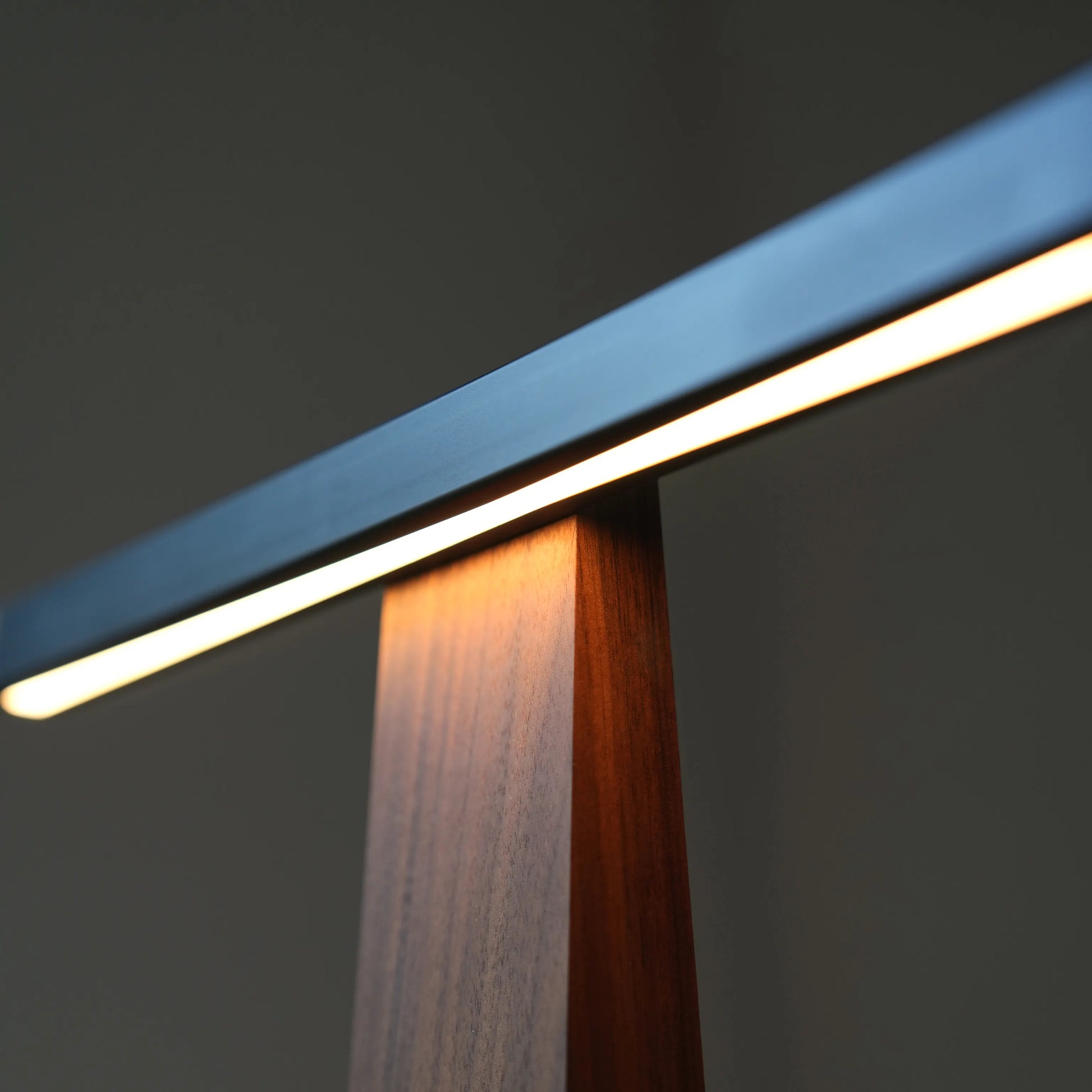 Close-up of integrated LED light strip and glowing walnut base of a modern lamp.