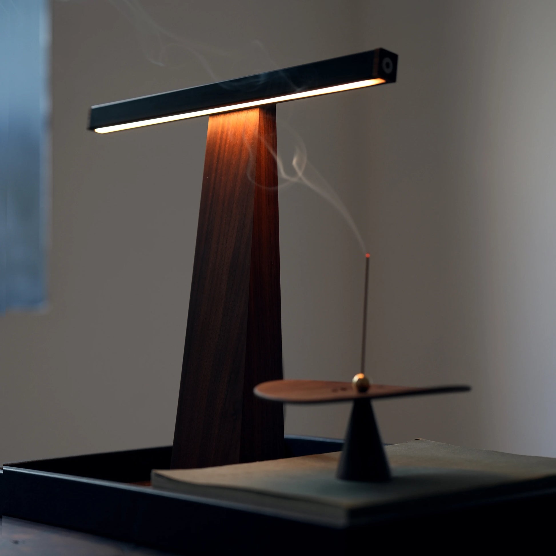 Low-light shot of the walnut lamp next to a stick incense holder with smoke.