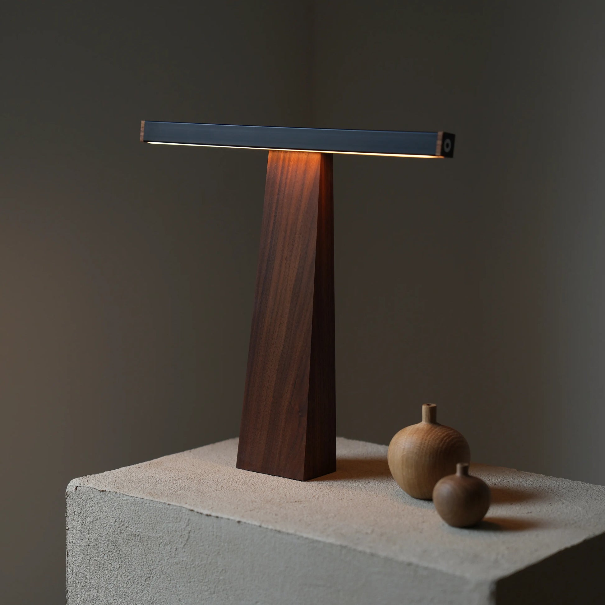 Sculptural LED lamp positioned on a concrete block with small wooden vase.