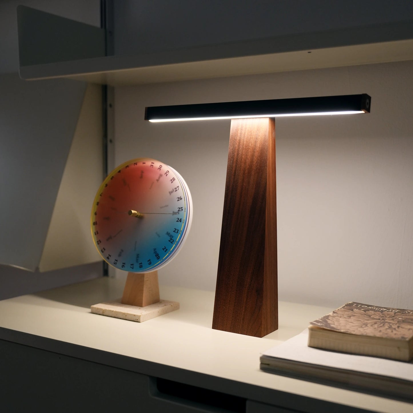 Walnut lamp on a shelf next to a colorful circular calendar.