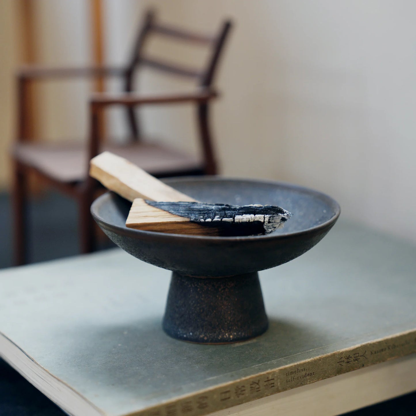 Black ceramic Palo Santo holder sitting on a book with a chair behind.
