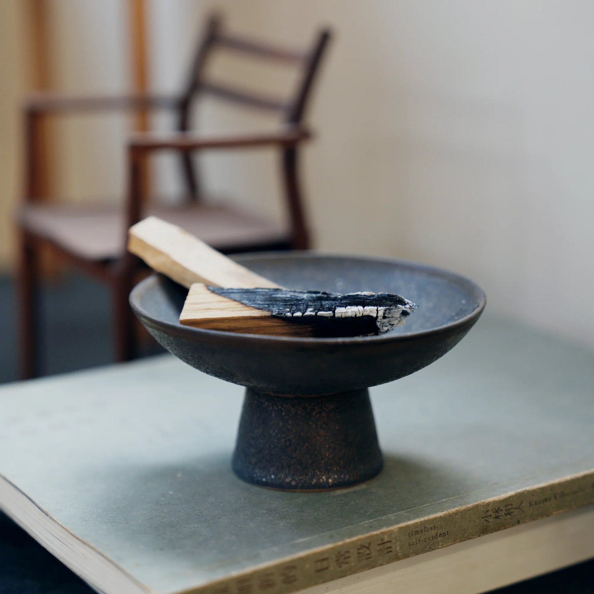 Black ceramic Palo Santo holder sitting on a book with a chair behind.