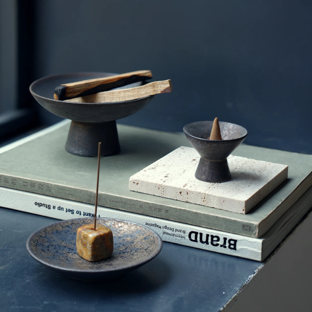 Wabi-sabi style incense holders displayed on stacked books.