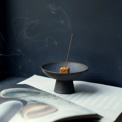 Stick incense burning in a stone holder placed in a ceramic dish.