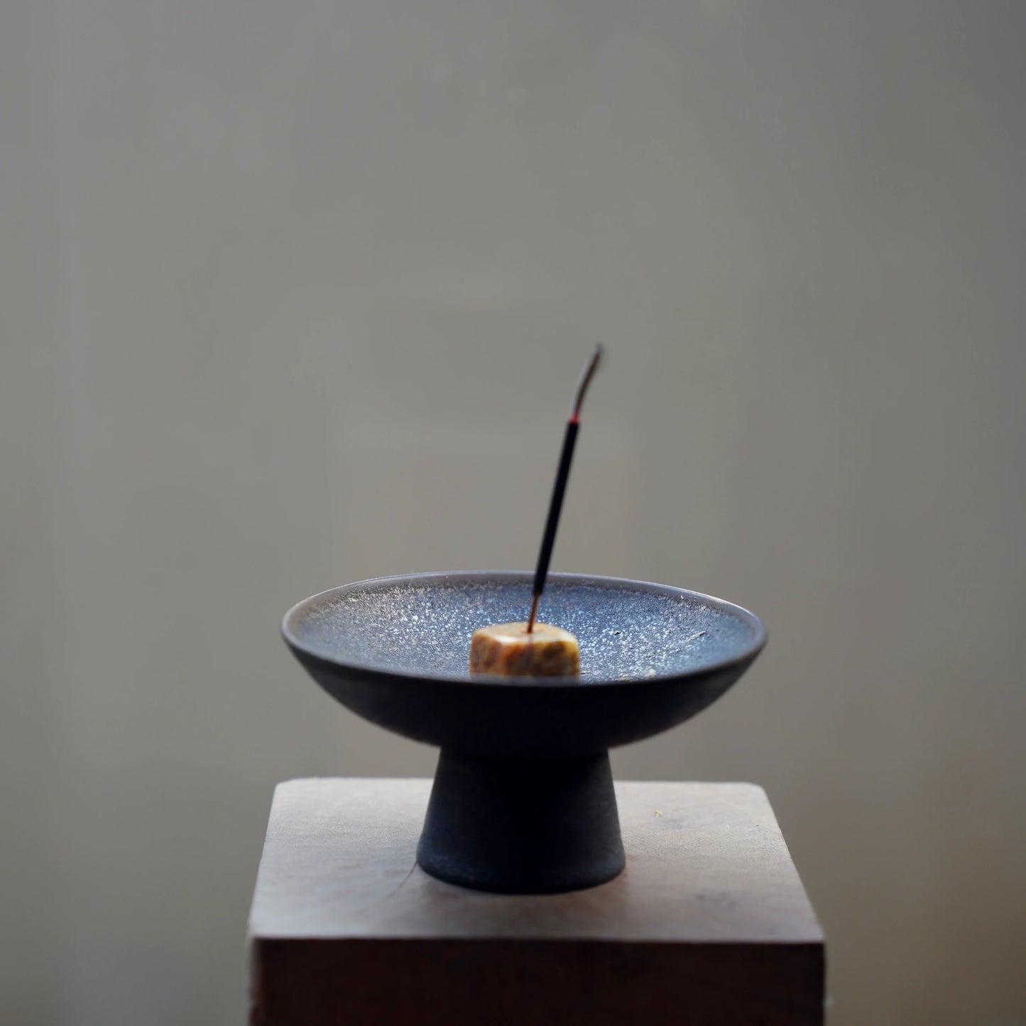 Incense stick in a stone holder inside a black ceramic ash catcher.
