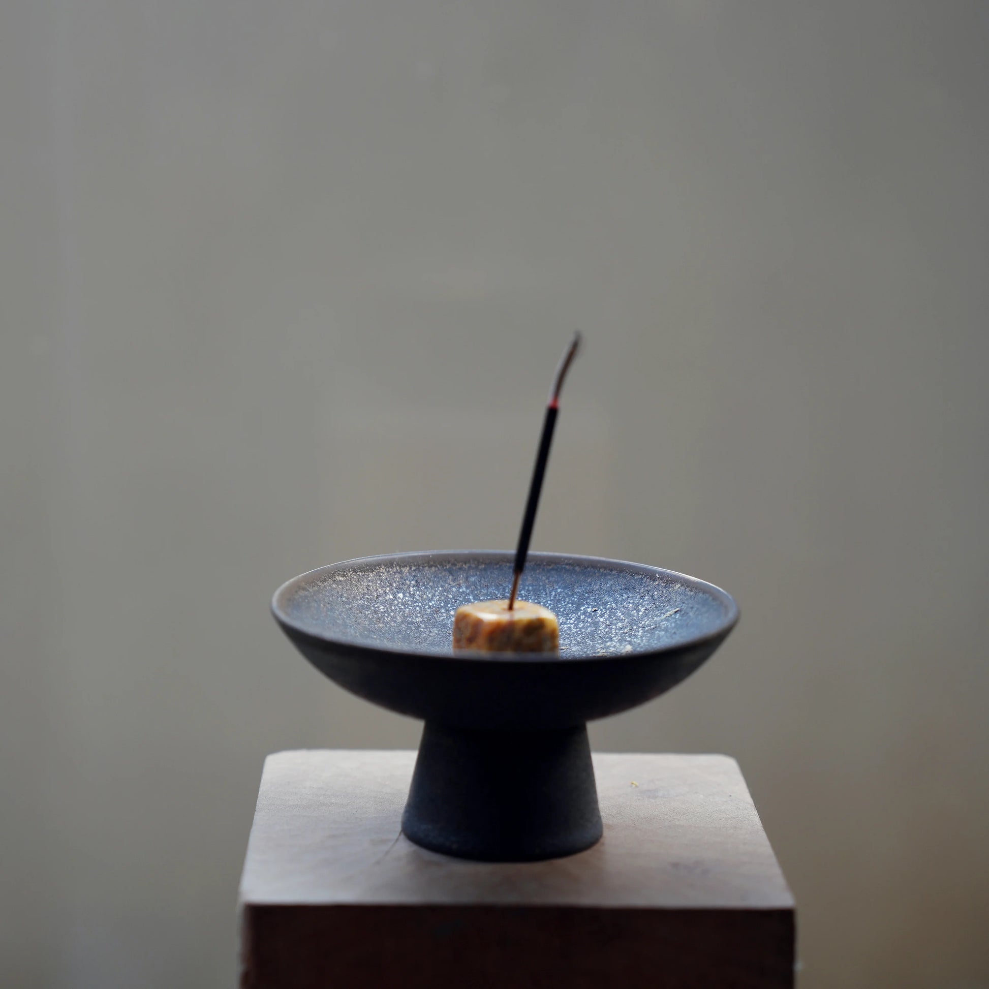 Incense stick in a stone holder inside a black ceramic ash catcher.