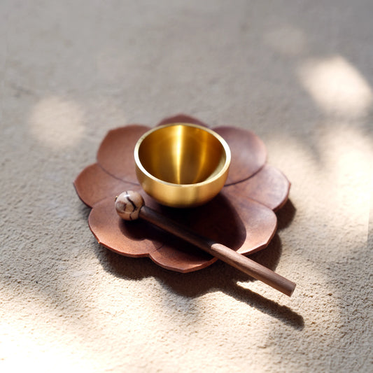 Mini singing bowl with sandalwood lotus base in a beam of sunlight.