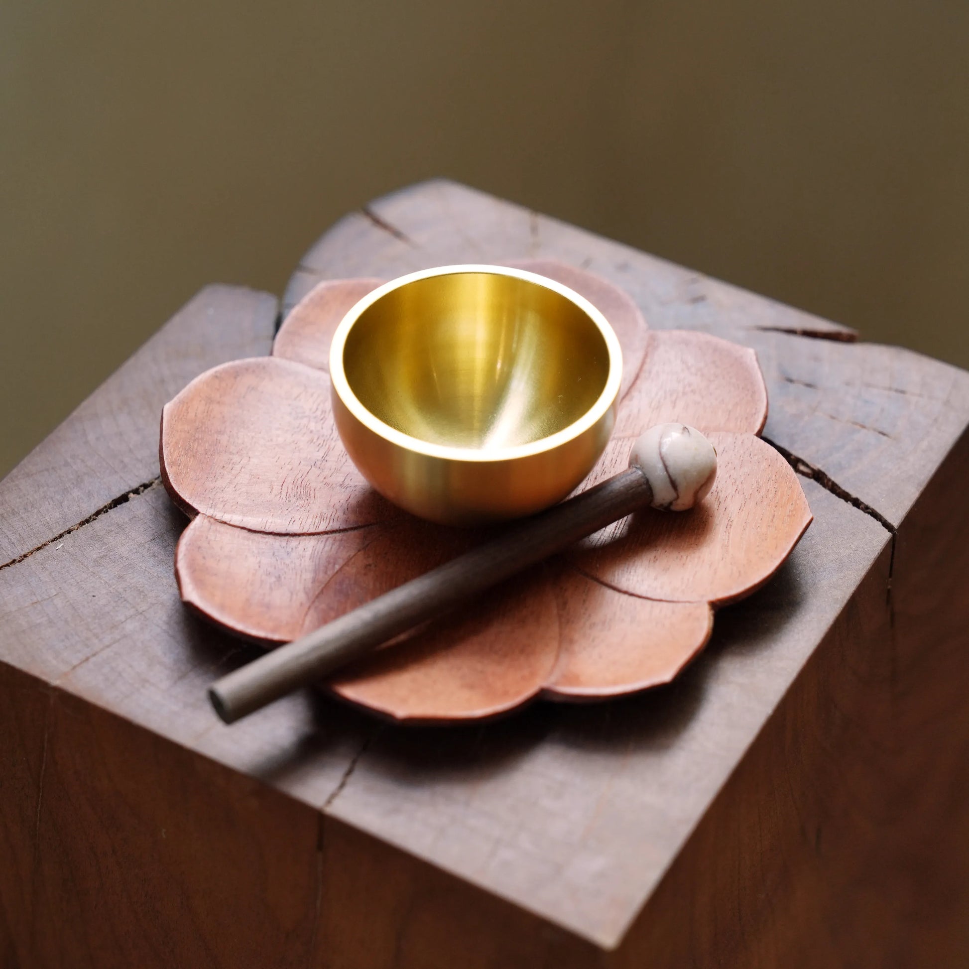 Small brass singing bowl and striker on a carved wooden lotus base.