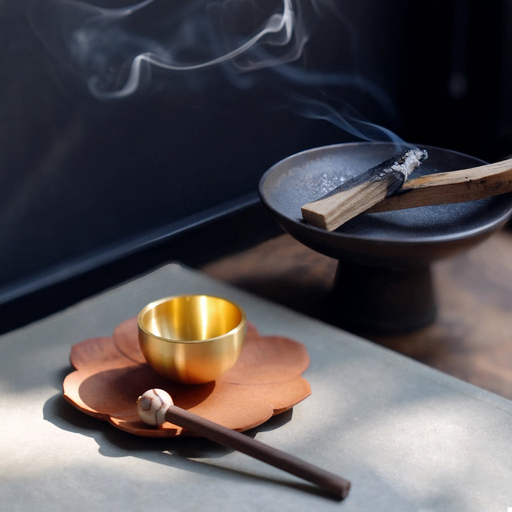 Mini singing bowl next to a palo santo incense burner with smoke.