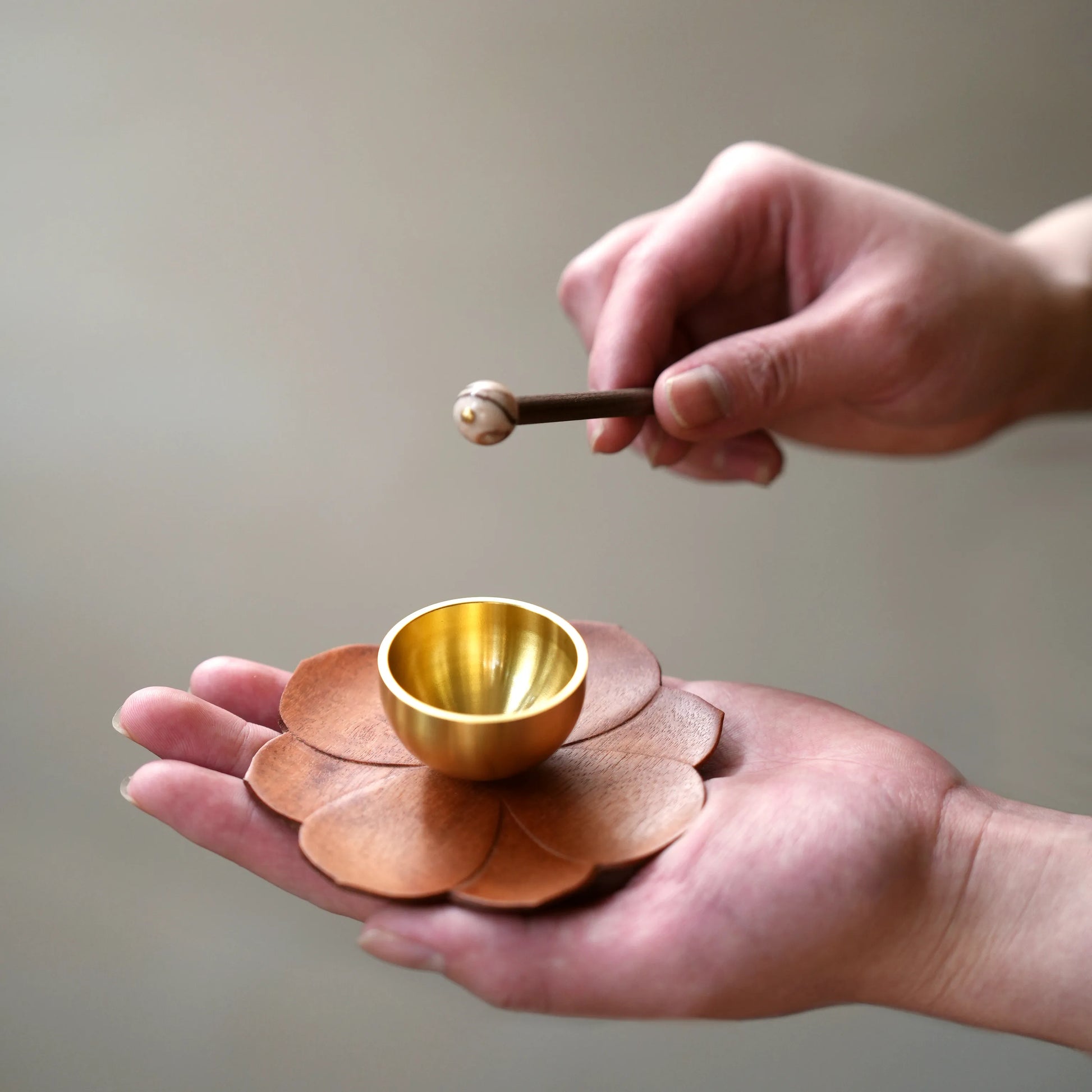 Hands holding a mini meditation chime bowl on a lotus-shaped base.