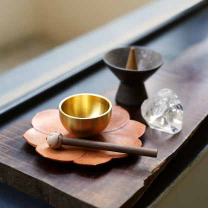 Small brass singing bowl set next to an incense cone and crystal.