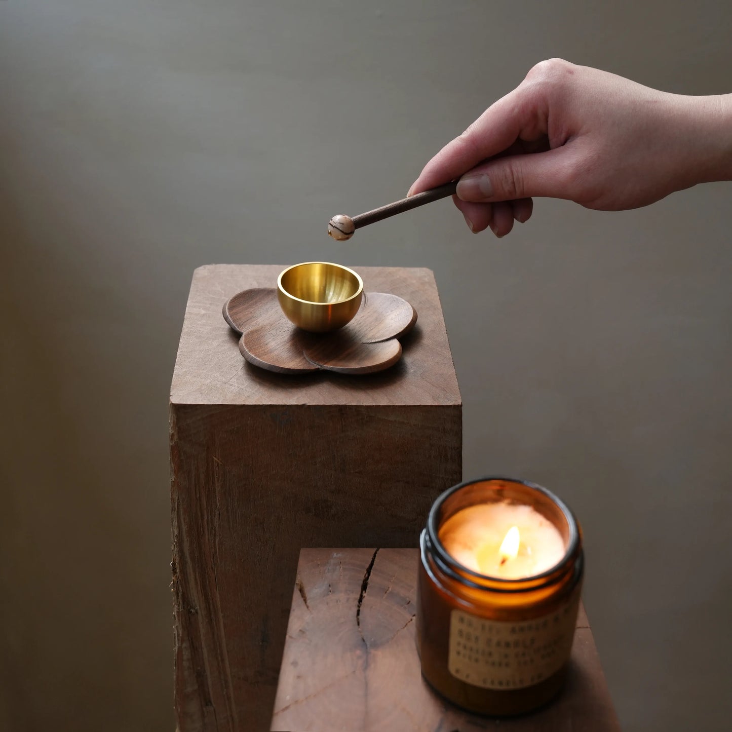 Hand holding a striker over a small singing bowl next to a candle.