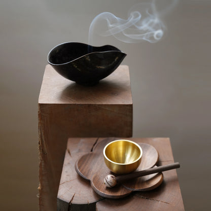 Small brass singing bowl set on a wood block with incense smoke.