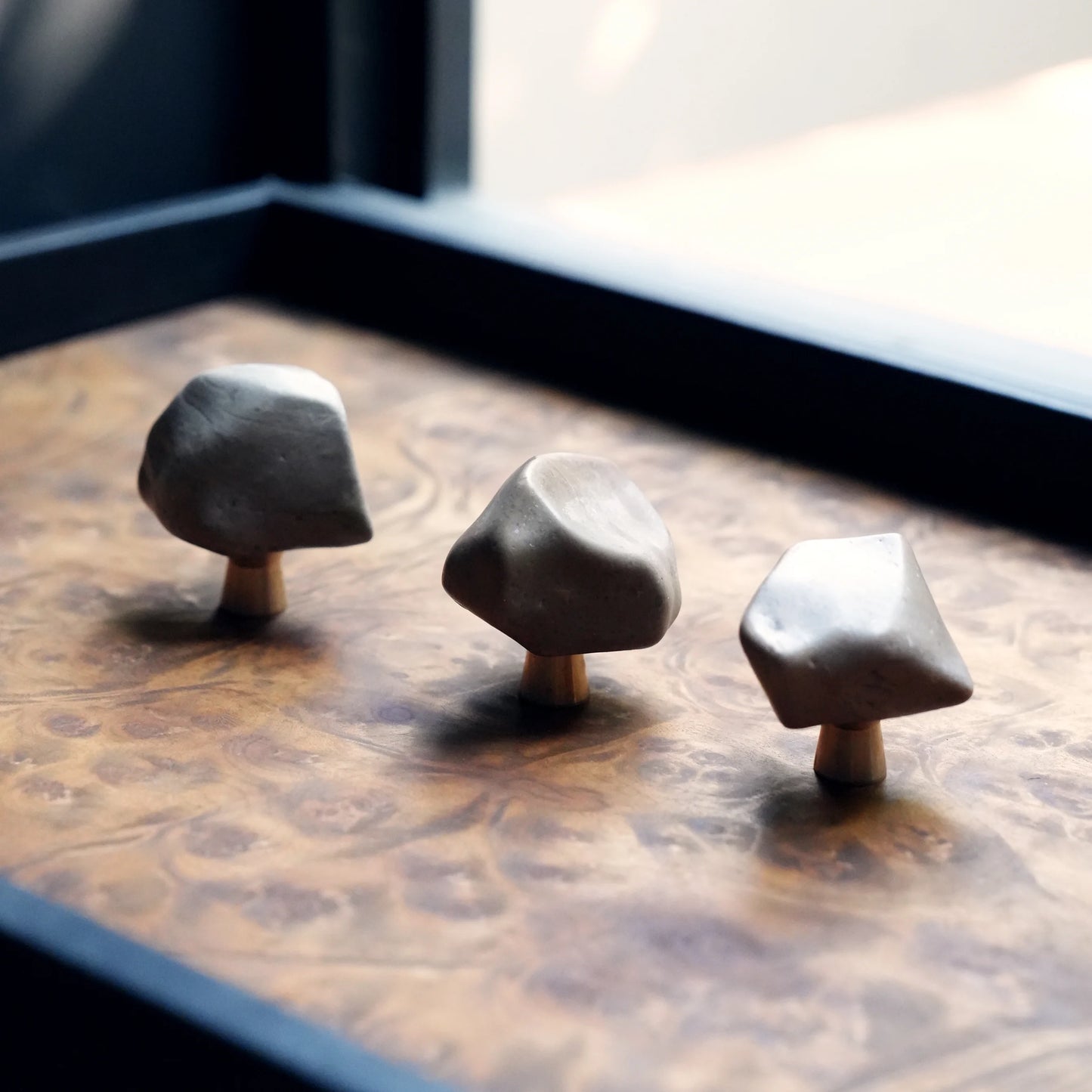 Three organic Gobi stone knobs on a burl wood tray by a window.