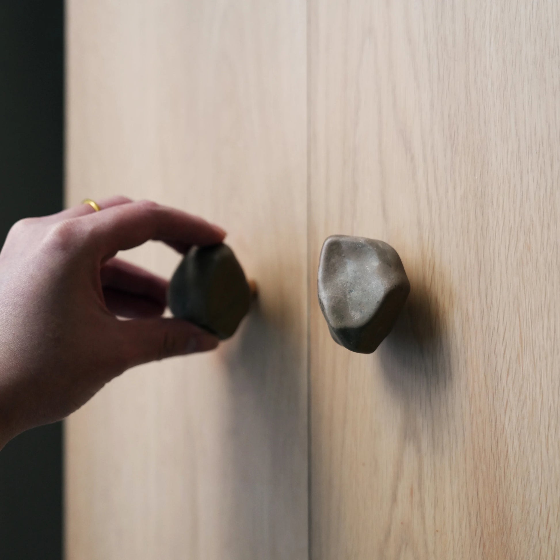 Hand turning a Gobi stone cabinet knob on a light wood cabinet door.