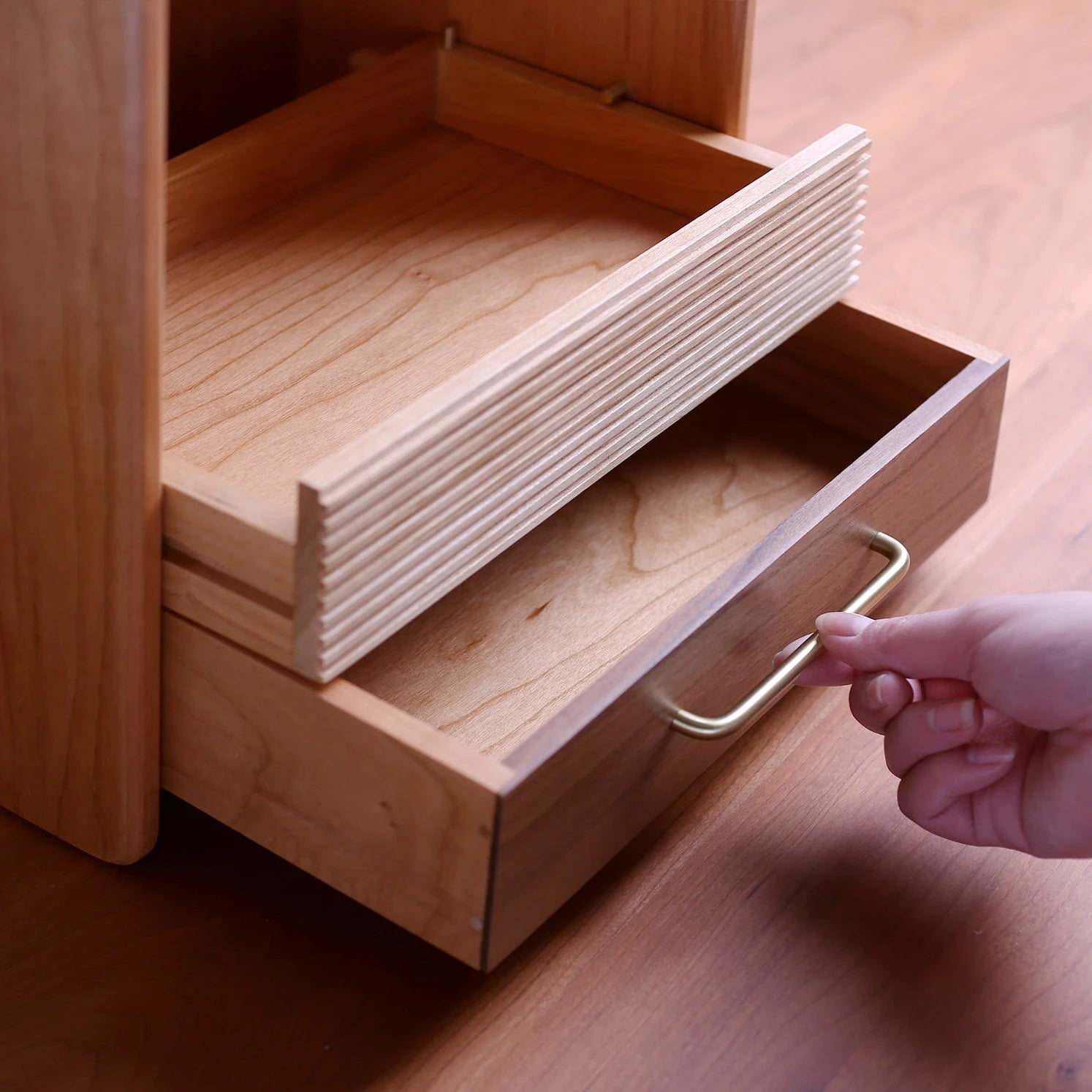 Hand pulling drawer of two-tone wood cosmetic organizer on a desk.