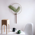 A modern wall vase with a palm leaf styled above a minimalist white table.