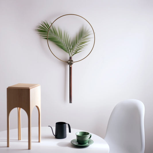 A modern wall vase with a palm leaf styled above a minimalist white table.