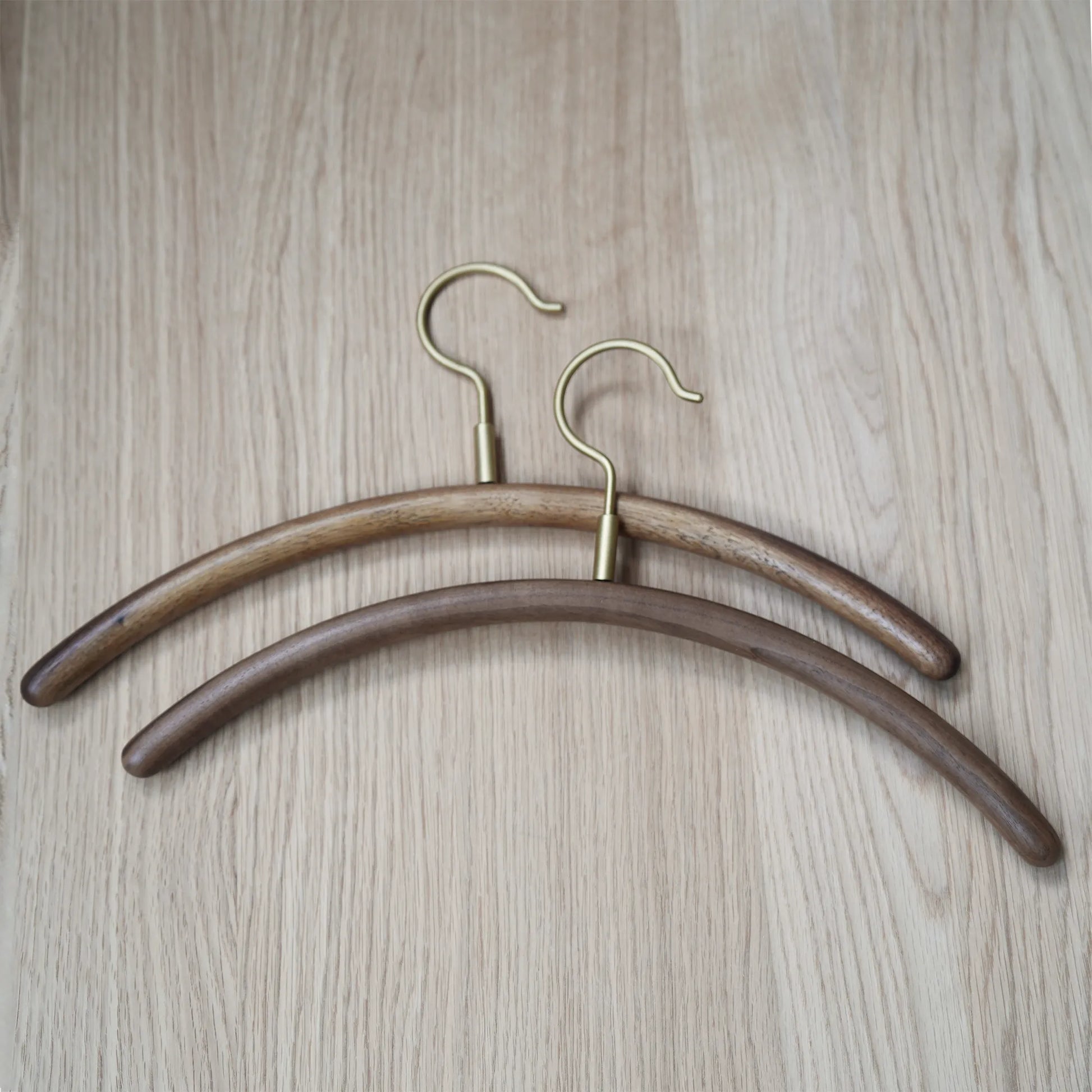 Two walnut clothes hanger with brass hooks on a wood table.