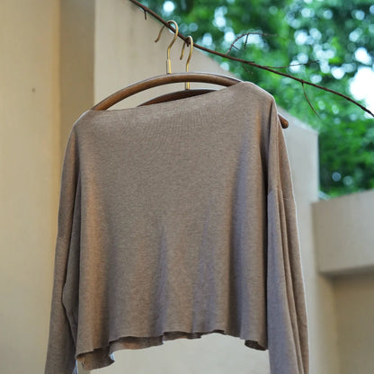 A wide-neck sweater hanging perfectly on a curved wooden hanger.