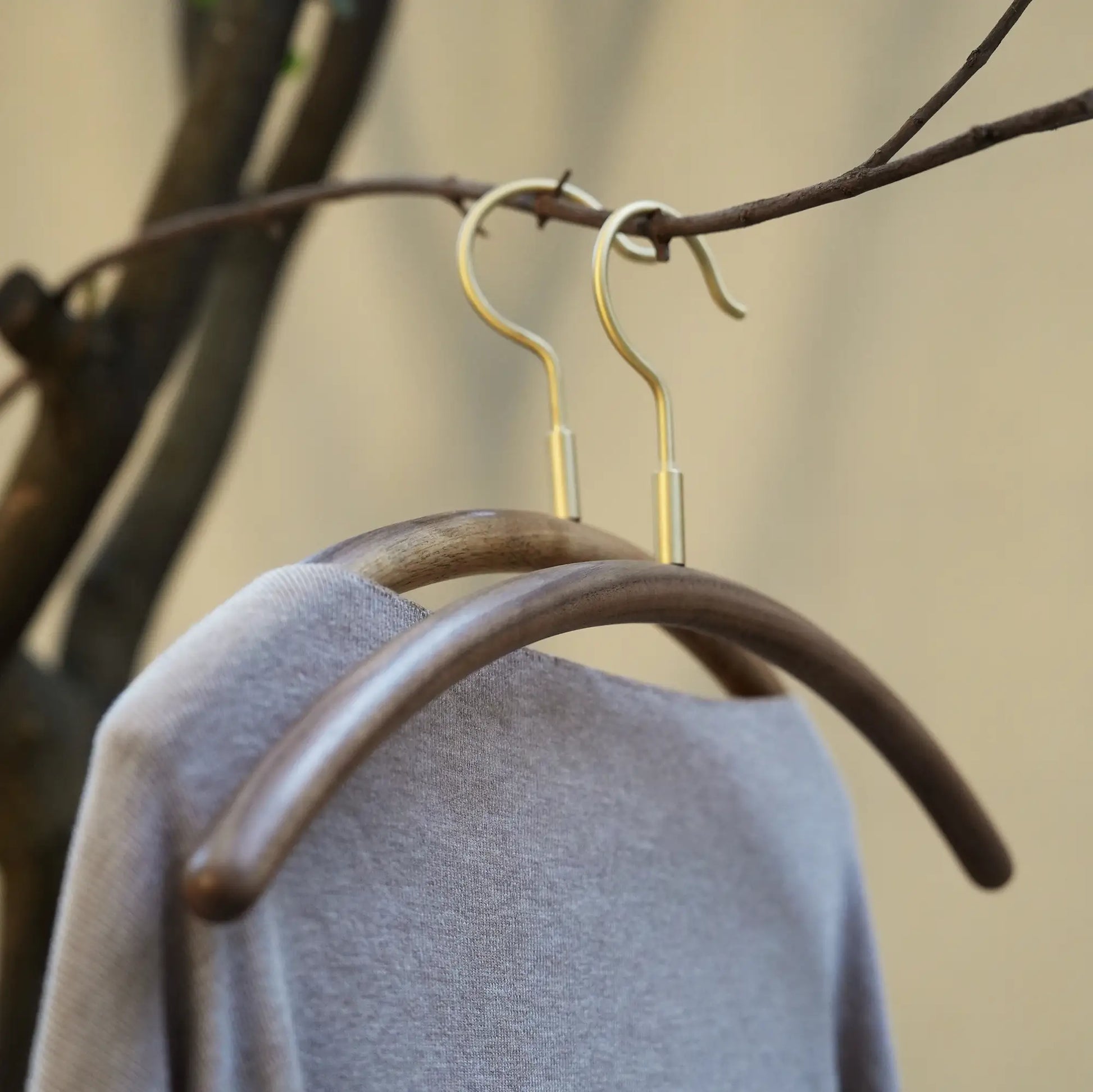 A soft grey sweater hanging on a curved walnut and brass clothes hanger.