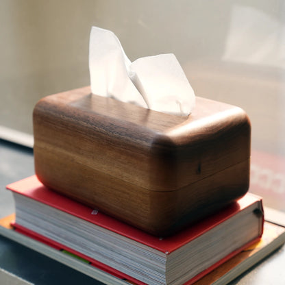 A modern wood tissue box cover styled on top of a red book.