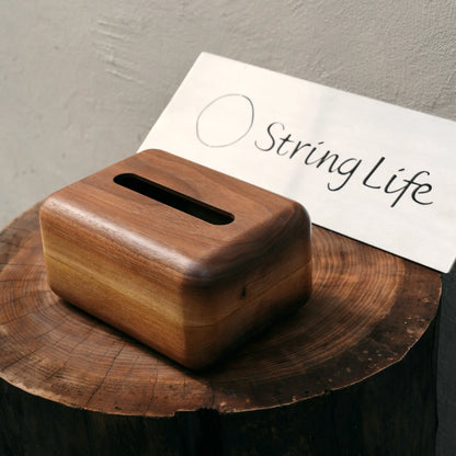 A minimalist walnut tissue box sitting on a natural wood tree stump.