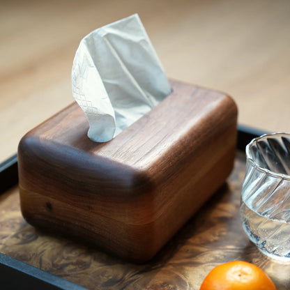 A dark wood tissue box on a tray with a glass and a tangerine.