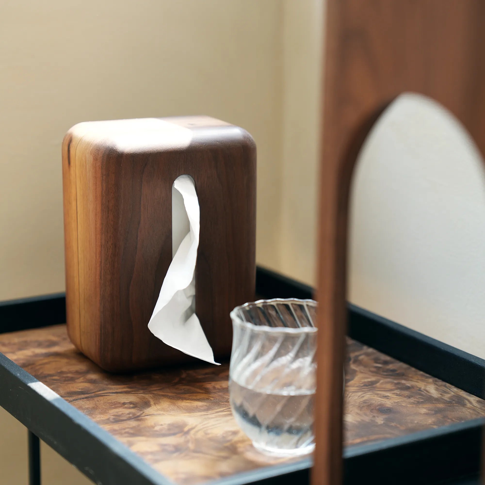 The vertical walnut tissue box cover on a modern tray with a water glass.