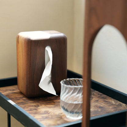 The vertical walnut tissue box cover on a modern tray with a water glass.