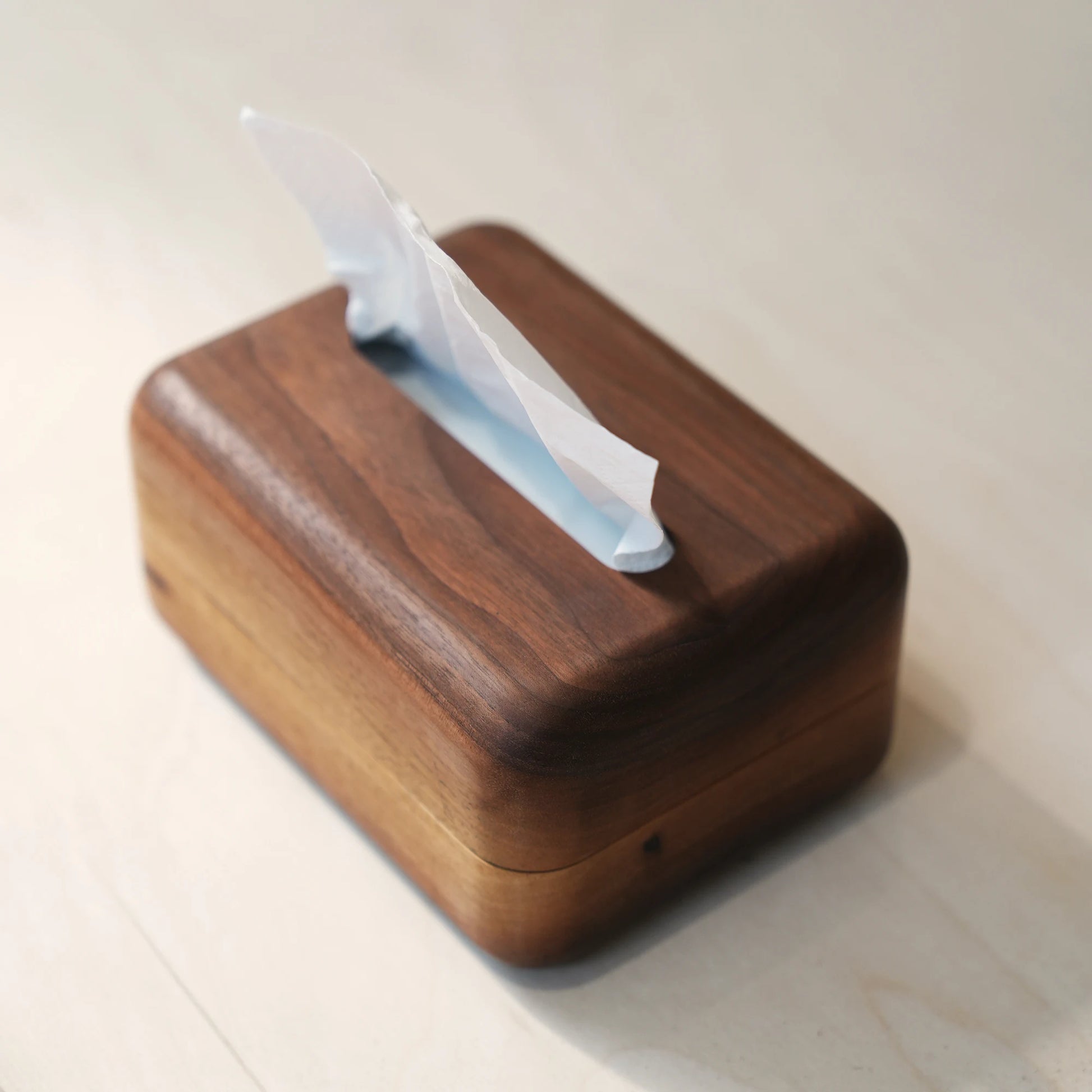 A dark walnut tissue box cover with soft rounded corners on a white desk.