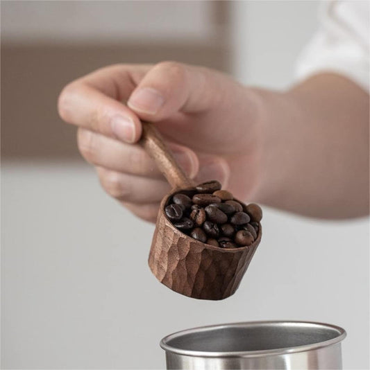 Hand holding the carved wooden scoop, full of fresh coffee beans.