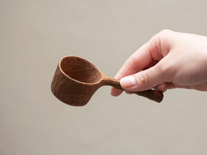 A person's hand holding the beautifully crafted walnut coffee spoon.