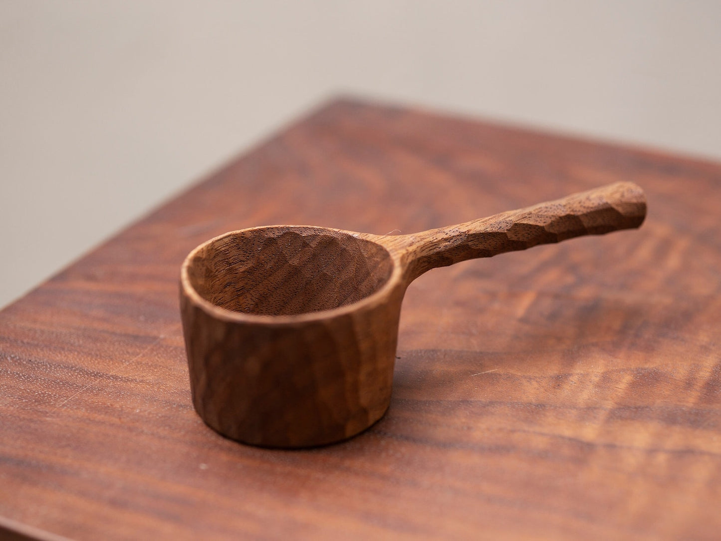 The dark, hand-carved coffee scoop styled on a rich wood surface.
