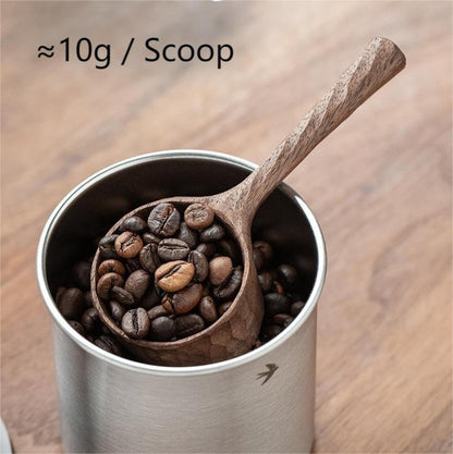 A walnut coffee scoop holding 10g of beans, resting in a coffee canister.